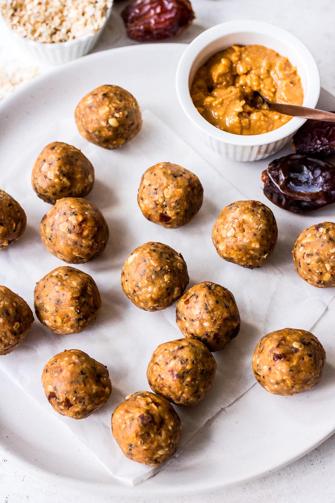White plate with energy balls, crunchy peanut butter, medjool dates and quick oats arranged on the plate