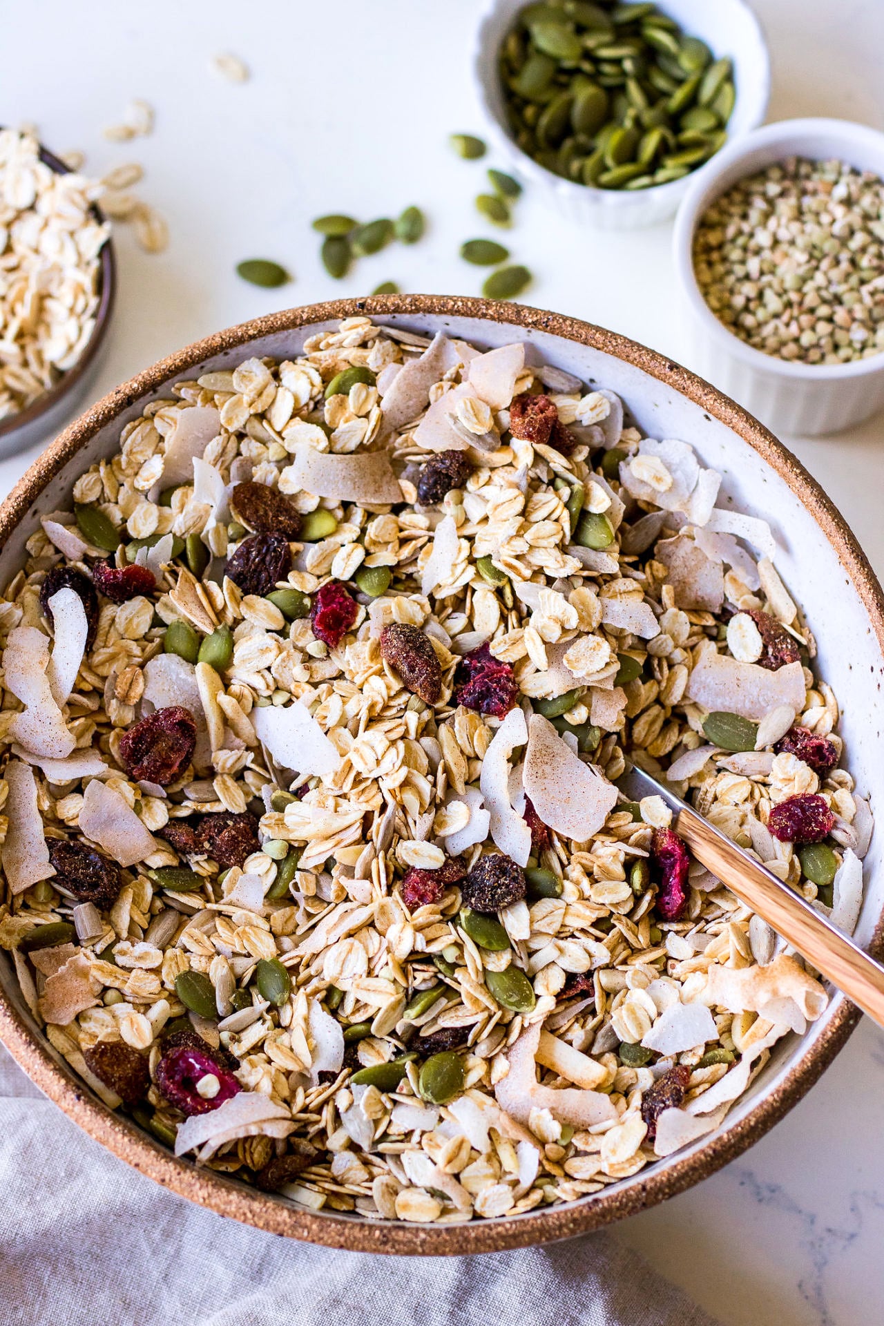 Large ceramic bowl filled with a healthy oat, coconut, pumpkin seed and dried fruit muesli with a wooden spoon sticking out
