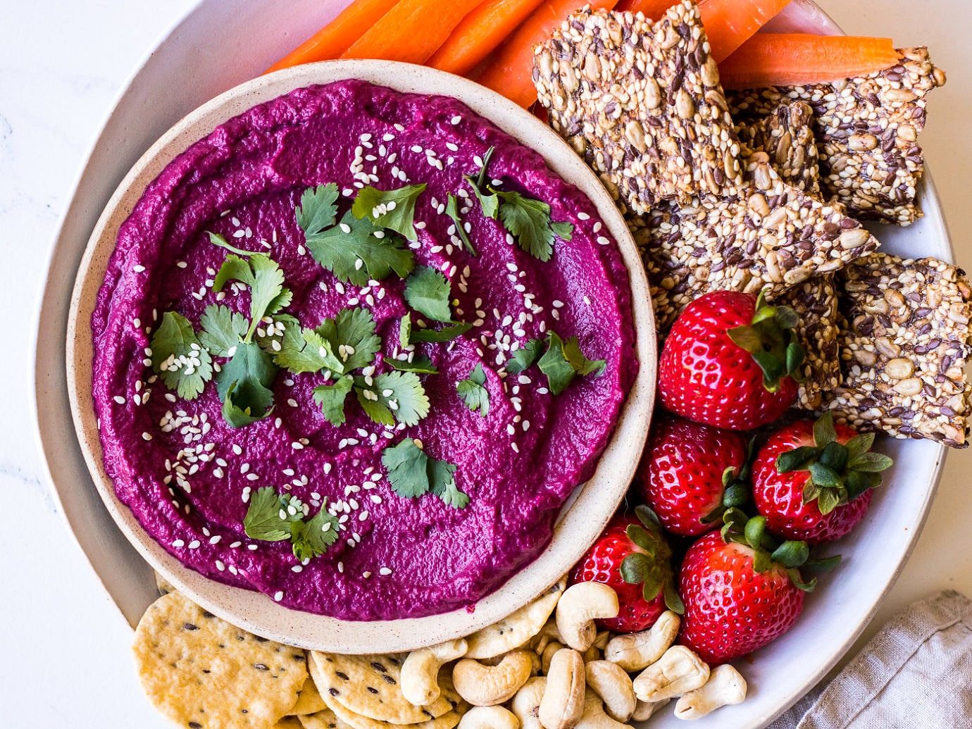 white ceramic plate snack platter with beet dip, seeded crackers, carrots and strawberries