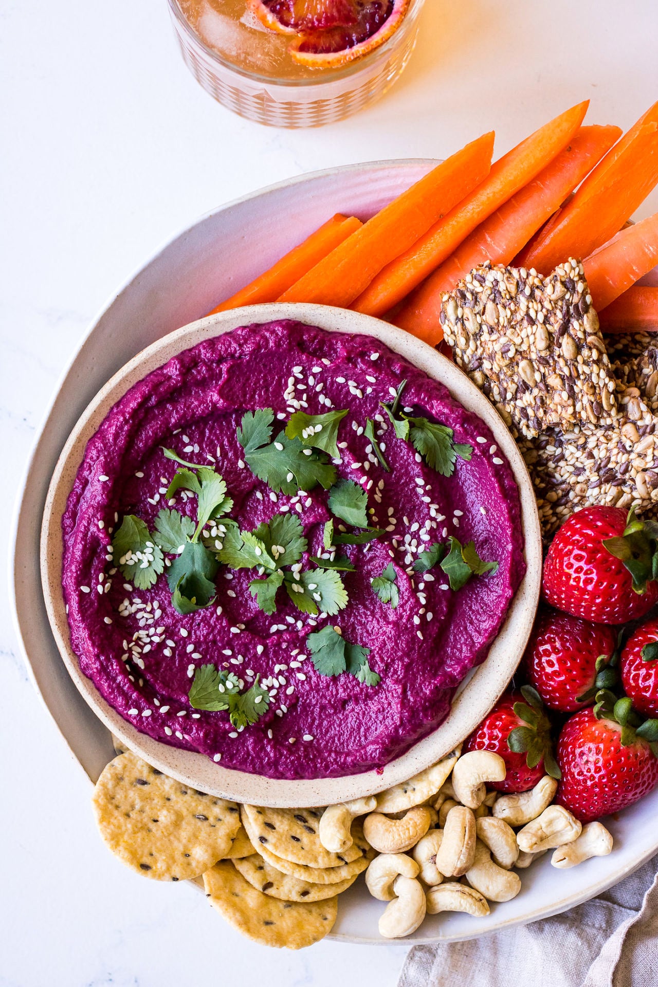 top view of snack platter with beetroot dip, carrot sticks, seeded crackers, cashews and strawberries