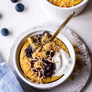 Vanilla mug cake in white ramekin with blueberries, yoghurt and shredded coconut, blue napkin and blueberries
