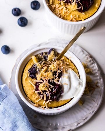 Vanilla mug cake in white ramekin with blueberries, yoghurt and shredded coconut, blue napkin and blueberries