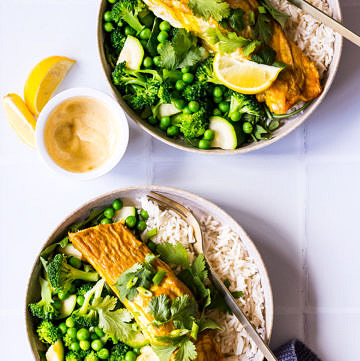 Top view two bowls of salmon, white rice, greens and peas with lemon and yoghurt