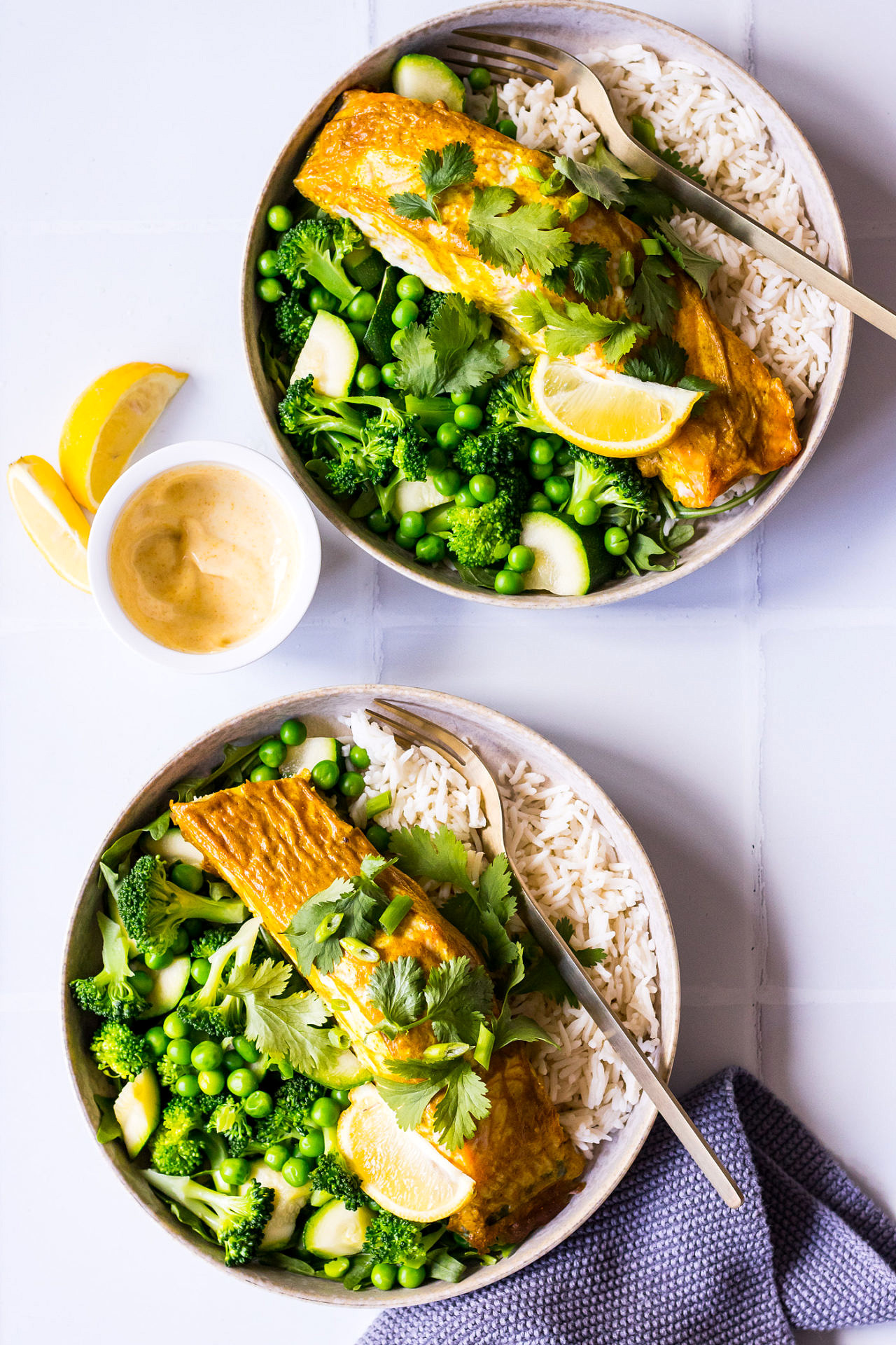 Top view two bowls of salmon, white rice, greens and peas with lemon and yoghurt