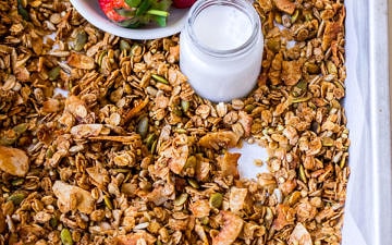 Baking tray with granola, strawberries, small jar of milk, wooden spoon