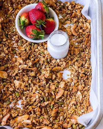Baking tray with granola, strawberries, small jar of milk, wooden spoon