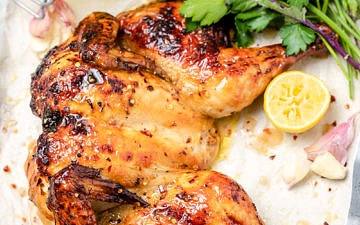 Flattened roast chicken with lemon pieces, fresh parsley and jar of pan juices