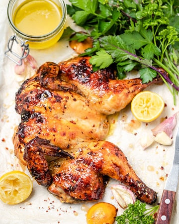 Flattened roast chicken with lemon pieces, fresh parsley and jar of pan juices
