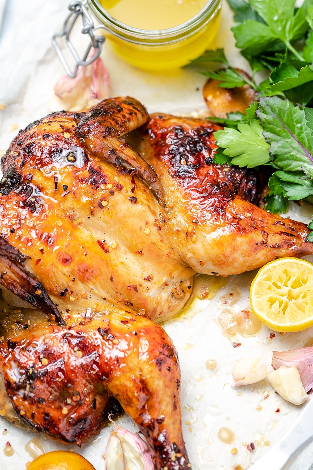 Close up of flattened chicken with lemon chilli and garlic, fresh herbs to side