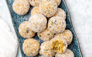 Blue rectangular plate with apricot bliss balls on top rolled in coconut, white table background