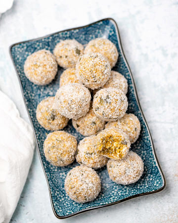 Blue rectangular plate with apricot bliss balls on top rolled in coconut, white table background