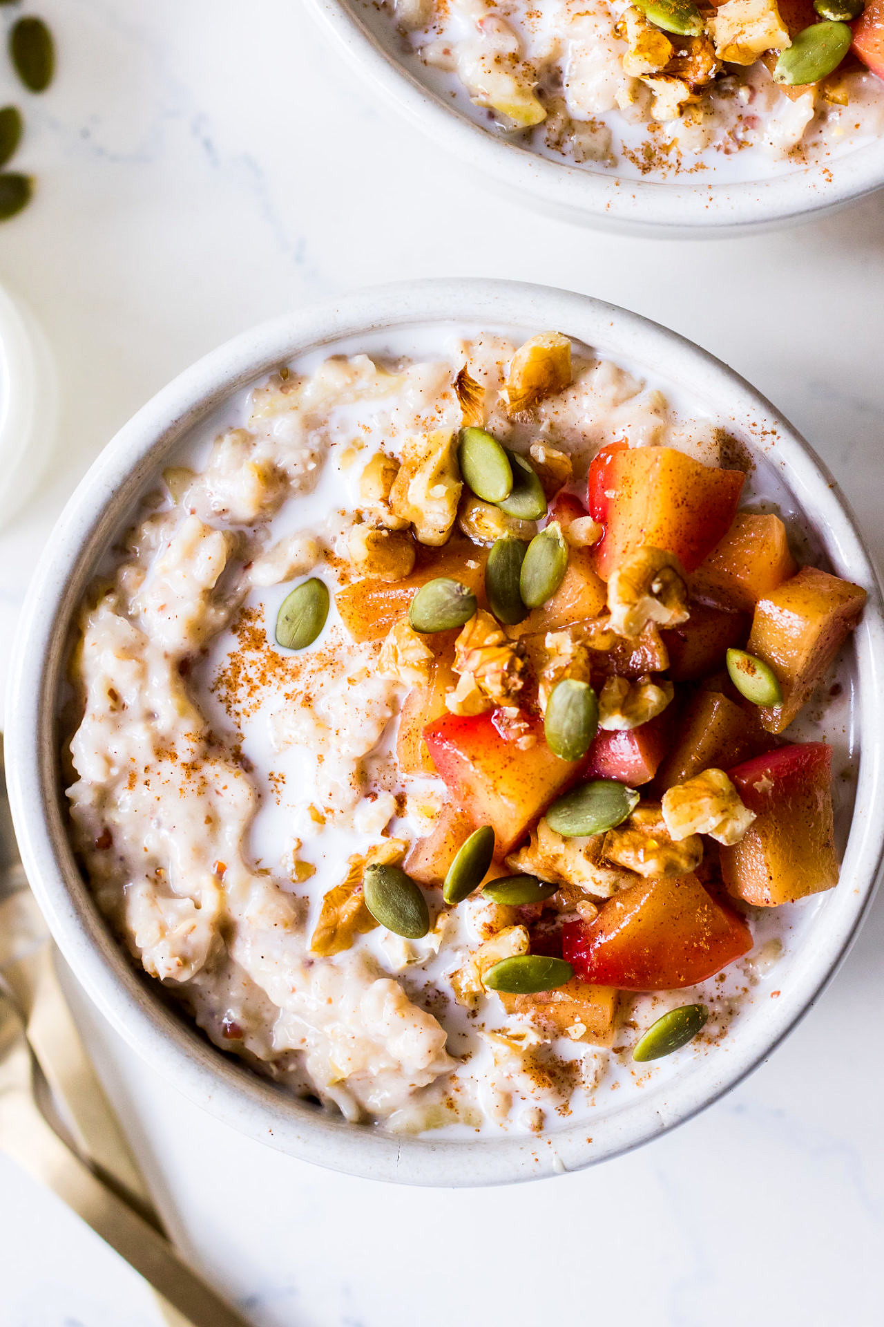 Top view two bowls of oatmeal with cinnamon, pan fried apples and walnuts crumbled on top