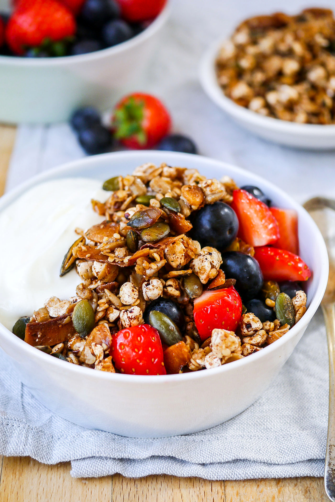 side view of a small blue bowl with Greek yoghurt, toasted muesli and berries on a wooden table