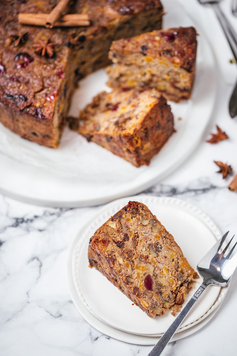 Sliced healthy Christmas cake with single slice on the side in foreground, white plates