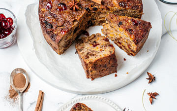 Christmas fruit cake on a white plate partly sliced, one slice on a side plate with fork