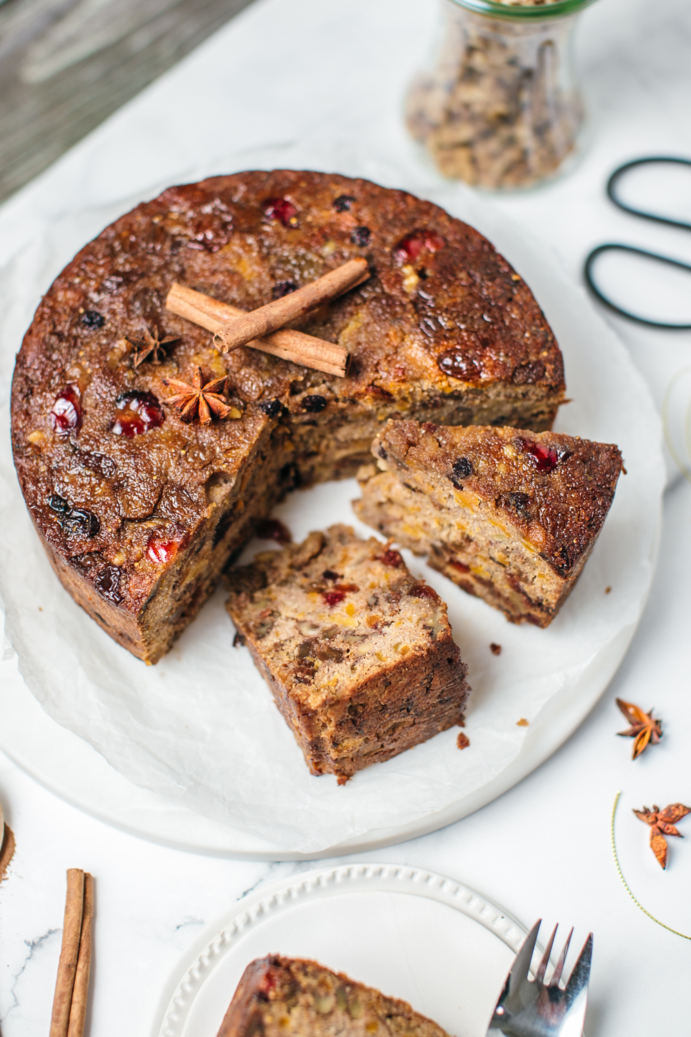 Partly sliced Christmas cake on a round white plate with cinnamon sticks on top