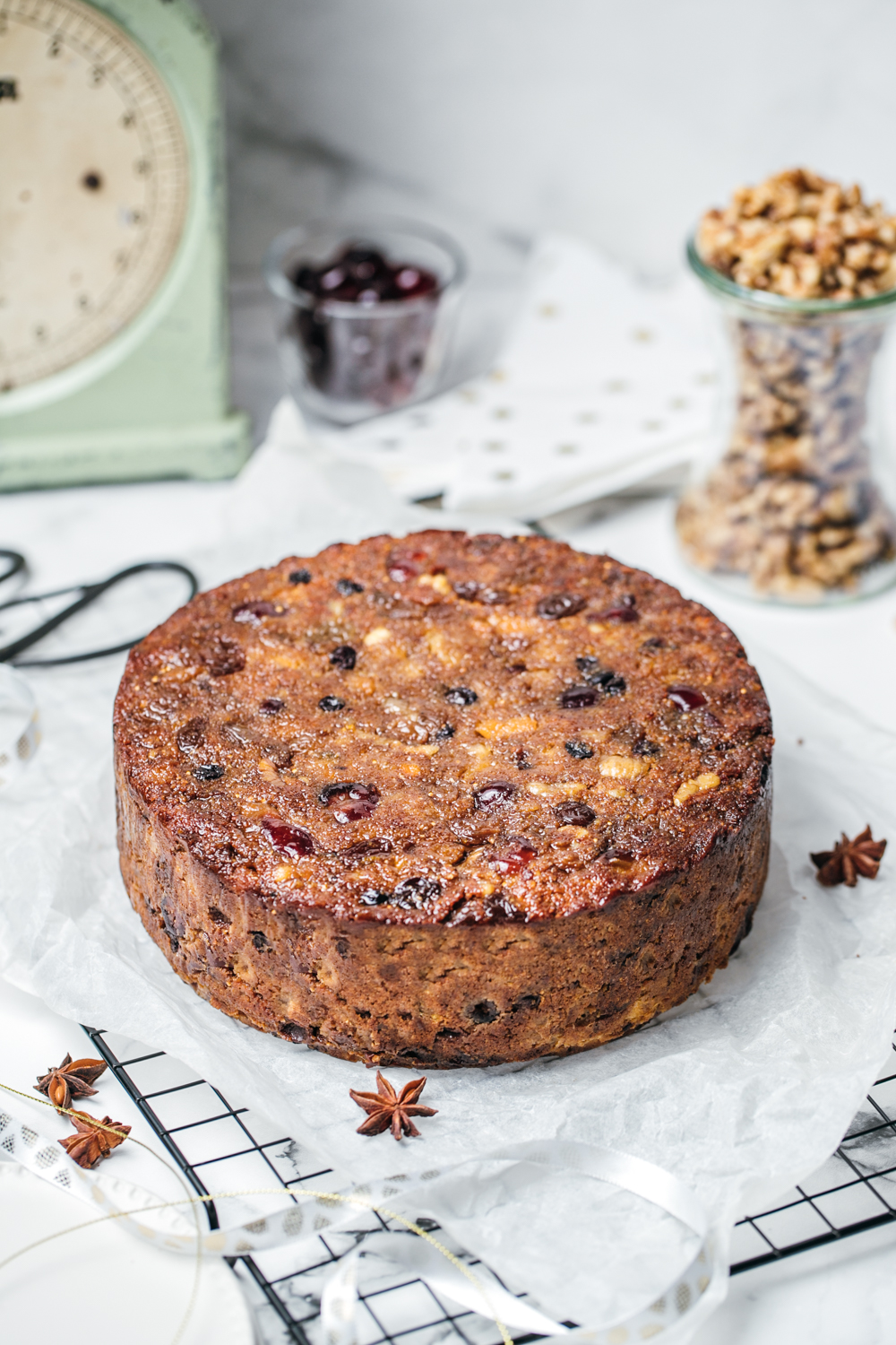 Healthy Christmas fruit cake on top of baking paper and wire rack, ingredients and scales in background