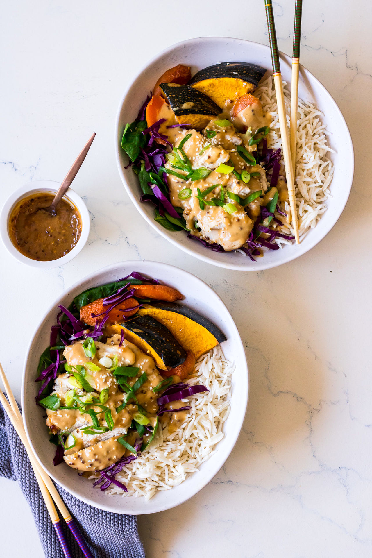Two white irregular bowls with rice, pumpkin, cabbage, chicken, miso mustard dressing, fresh herbs, chopsticks on side