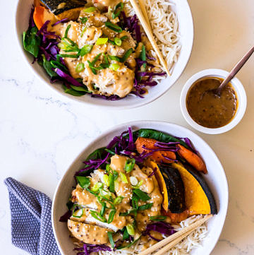 Two irregular white ceramic bowls with rice, roasted vegetables, purple cabbage, chicken and miso mustard dressing