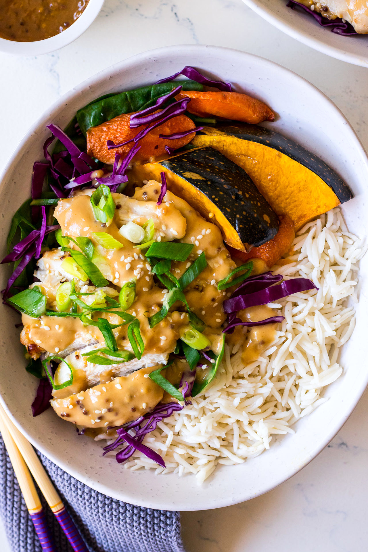 White ceramic bowl with white rice, pumpkin, cabbage, chicken, spring onion and miso mustard creamy dressing