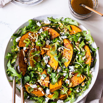 White ceramic bowl with rocket, roast pumpkin and goats cheese salad, balsamic dressing jar to side
