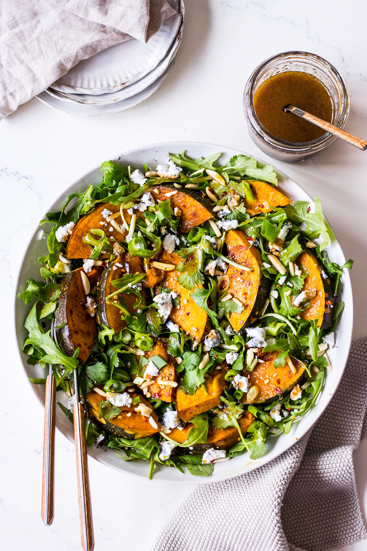 White ceramic bowl with rocket, roast pumpkin and goats cheese salad, balsamic dressing jar to side