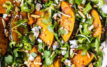 Round white ceramic dish filled with a salad of rocket, pumpkin, chilli, almonds, goats cheese and herbs