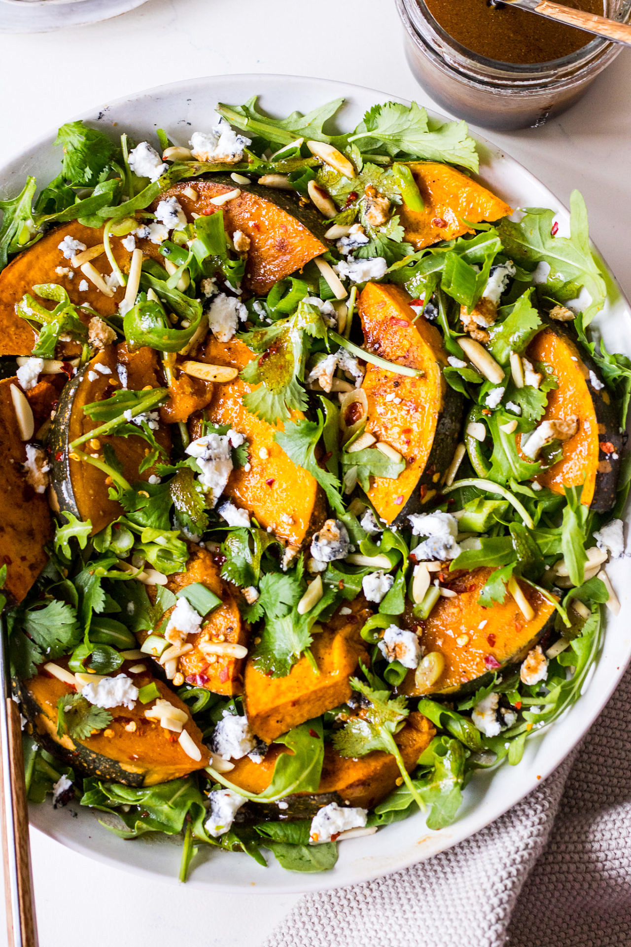 Round white ceramic dish filled with a salad of rocket, pumpkin, chilli, almonds, goats cheese and herbs