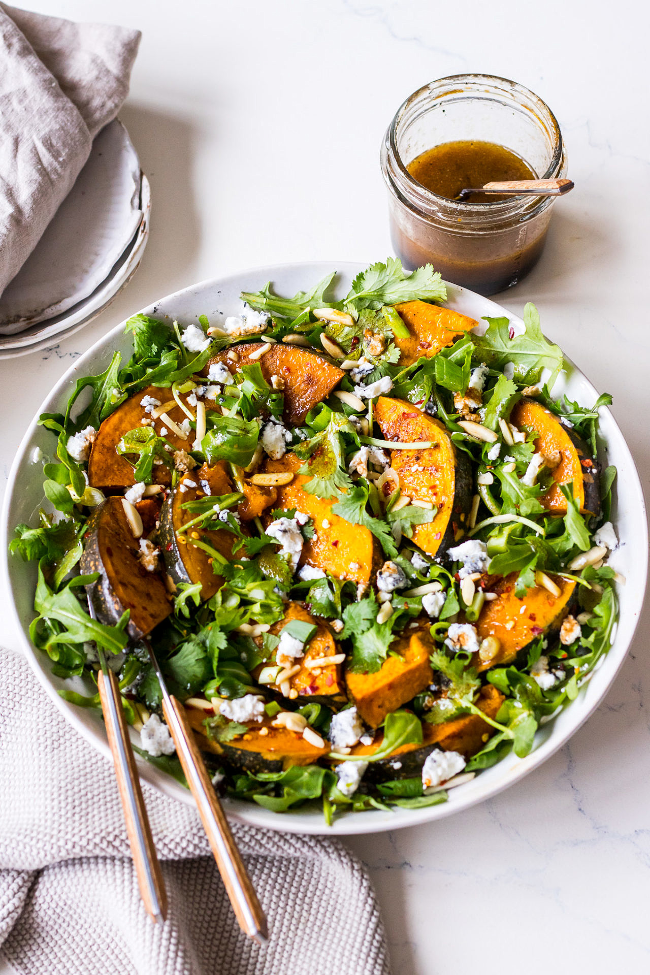 Rocket, pumpkin and goats cheese salad in a shallow ceramic bowl, small jar of balsamic dressing in the background