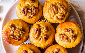 Pumpkin banana and walnut muffins arranged on small white ceramic plate, on top of neutral linen napkin