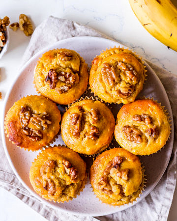 Pumpkin banana and walnut muffins arranged on small white ceramic plate, on top of neutral linen napkin