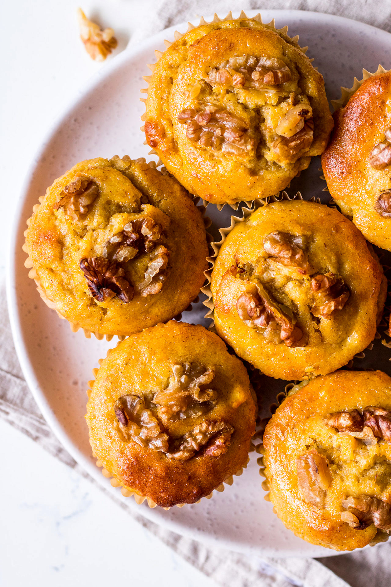 Close up plate of pumpkin, banana and walnut muffins, white ceramic plate on a linen napkin