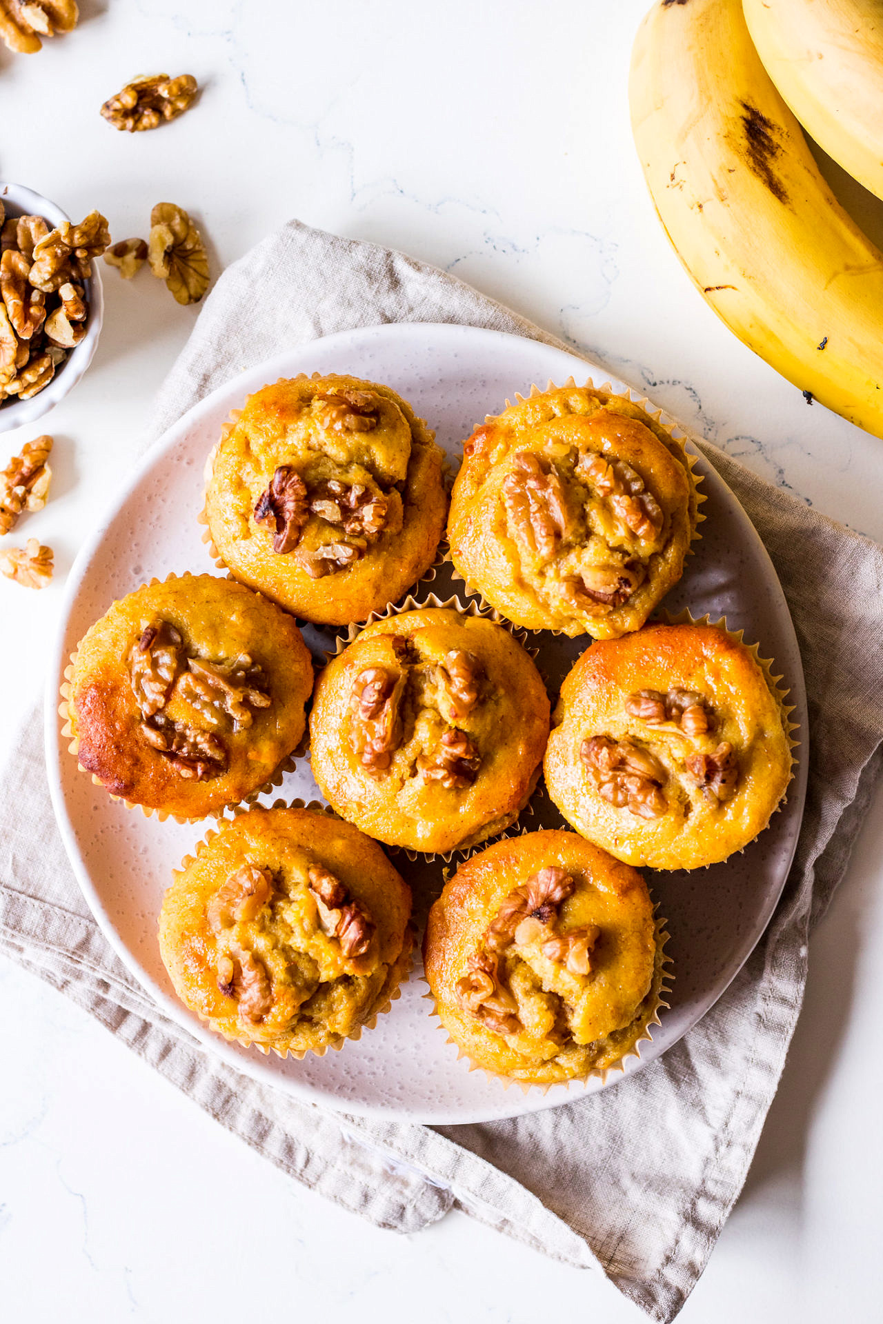 Small plate of pumpkin banana muffins topped with walnuts, arranged on a linen napkin