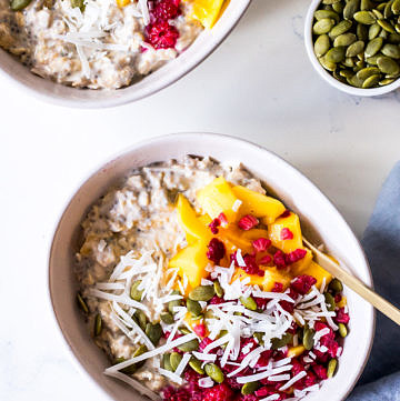 Two ceramic bowls with overnight oats, mango, coconut and raspberries