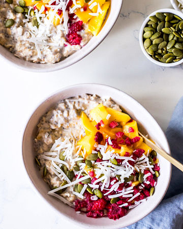 Two ceramic bowls with overnight oats, mango, coconut and raspberries