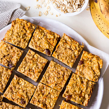 Banana oatmeal bars on a white plate with rolled oats and bananas