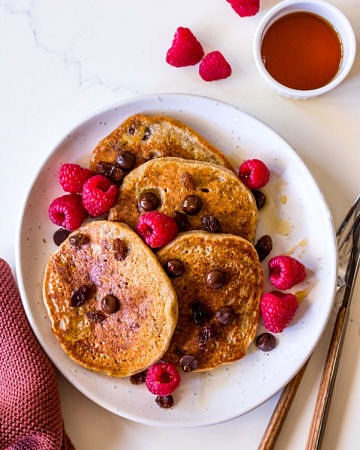 Vegan protein pancakes on white ceramic plate with chocolate chips, raspberries and maple syrup