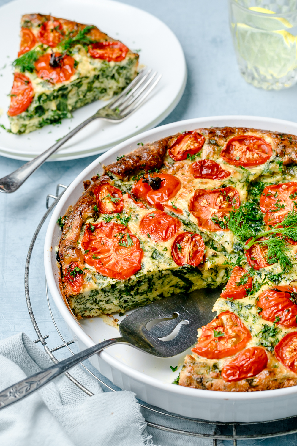 Side view of crustless ricotta kale pie in white baking dish sitting on top of a round cooling rack