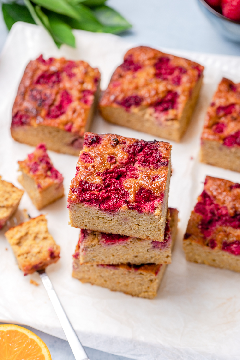 Squares of healthy orange almond cake stacked, topped with raspberries