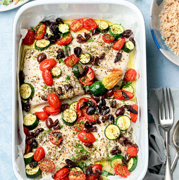 Fish tray bake with zucchini, tomato and olives on a blue background