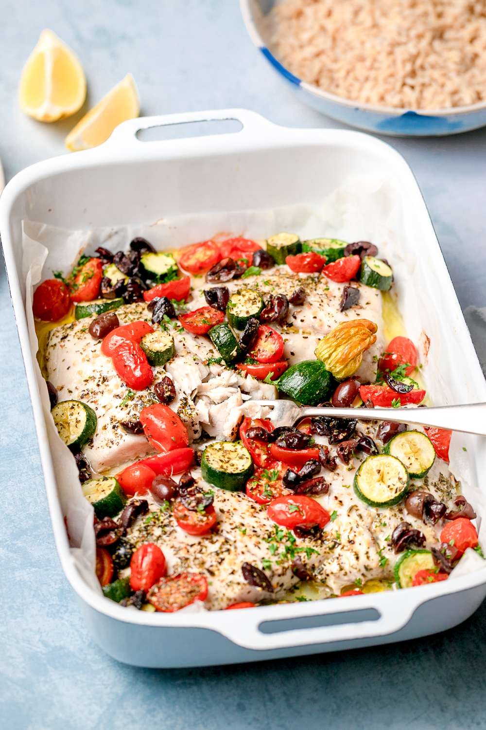 White oven dish with white fish, tomato, zucchini and olives, herbs