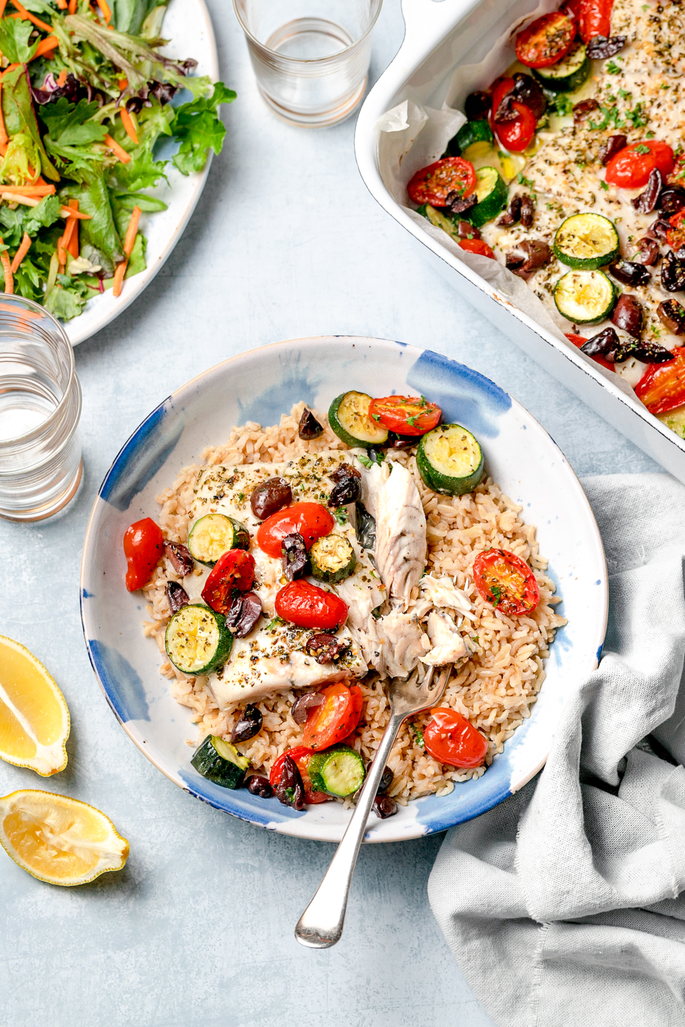 White fish, brown rice and vegetables in a bowl with sliver fork and lemon wedges