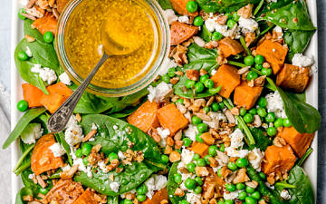 Salad of baby spinach, sweet potato and peas topped with feta, seeds and mustard dressing