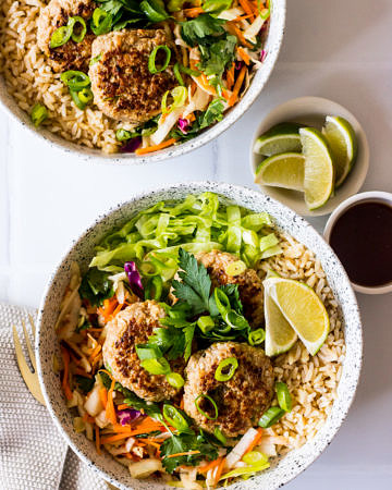 Speckled bowls with brown rice, pork patties, salad, herbs and lime