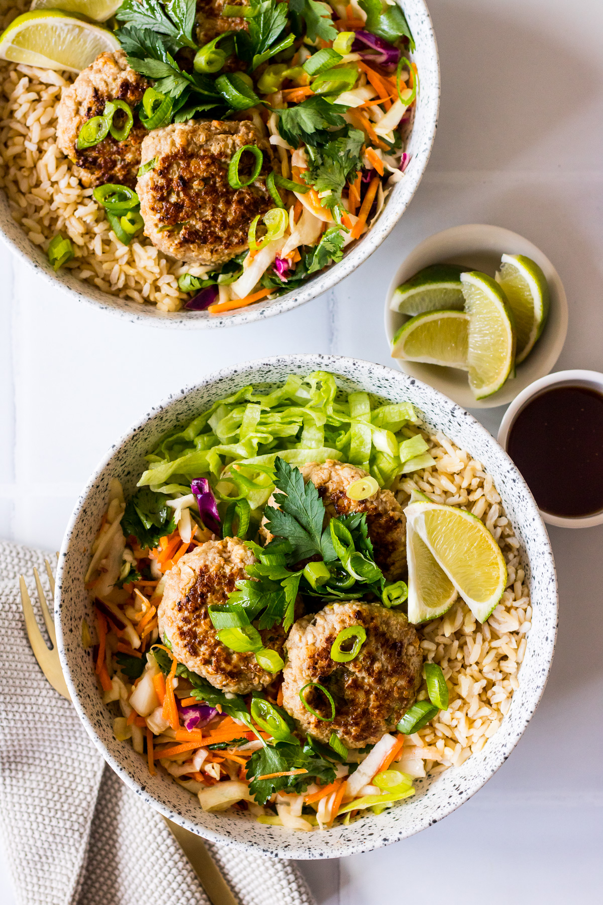 Speckled bowls with brown rice, pork patties, salad, herbs and lime