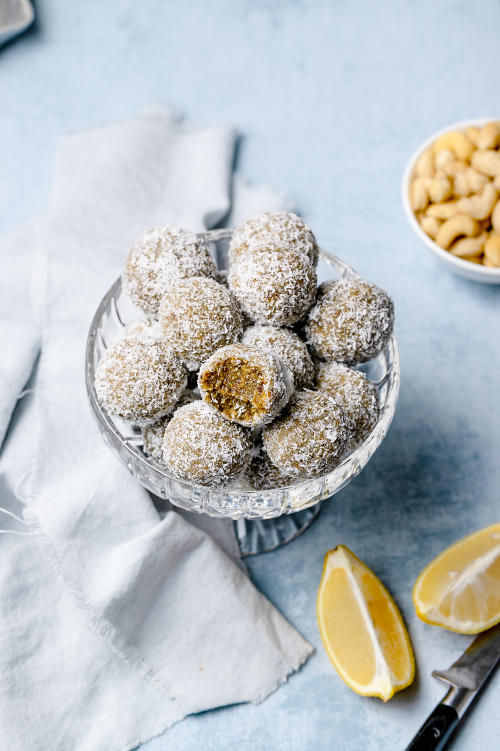Small glass bowl filled with energy balls rolled in desiccated coconut, lemon to the side