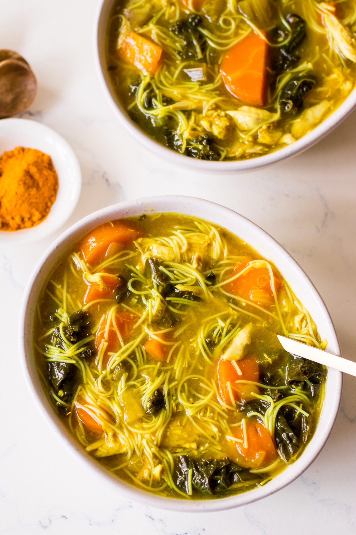 White ceramic bowl of turmeric chicken noodle soup with a gold spoon