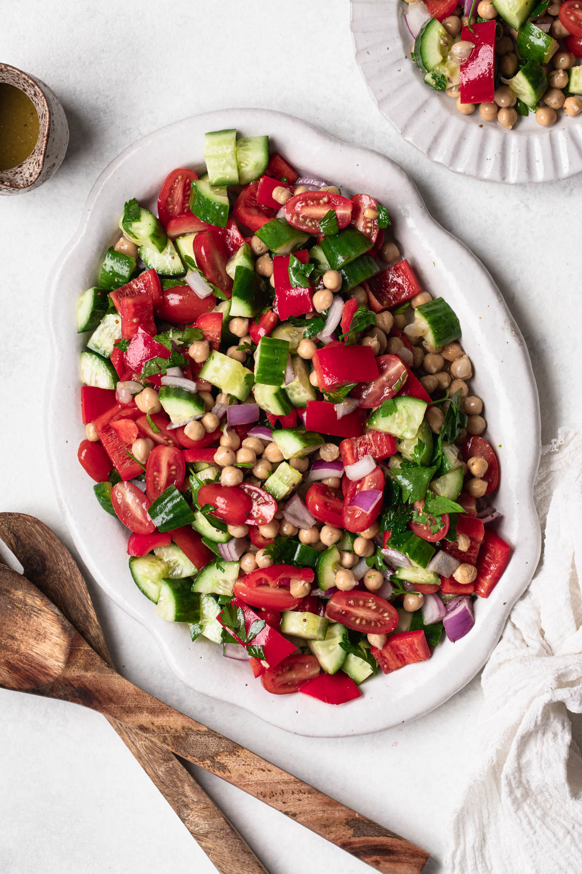 Chop salad on ceramic oval platter with wooden serving spoons and oil dressing