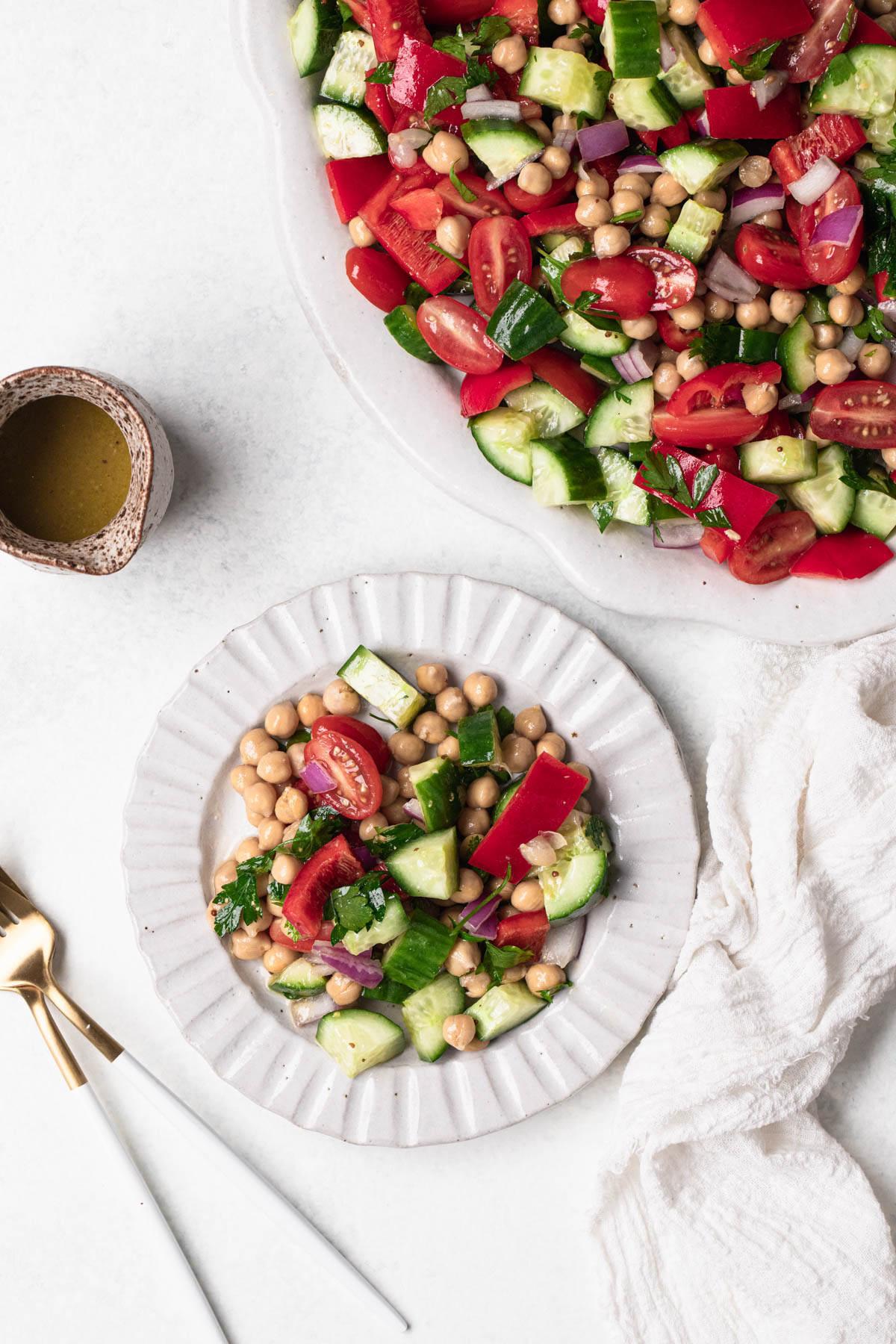 Serve of a chopped salad on a small white ridge plate, salad contains cucumber, tomato, capsicum, chickpeas, red onion and parsley