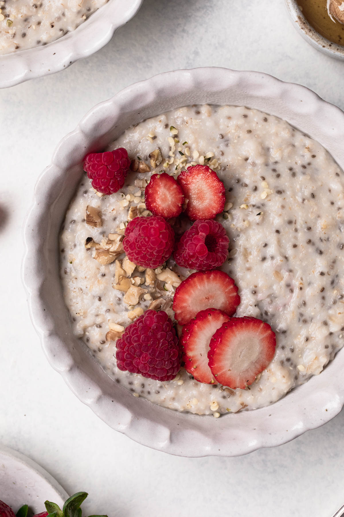 Close up of a white bowl of porridge with chia seeds, sliced strawberries and walnuts.